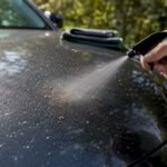 Hand spraying bug remover on car bonnet