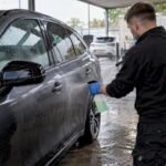 Detailer spraying wet car panel before rinsing