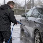 Driver rinses winter salt from car wheel arches